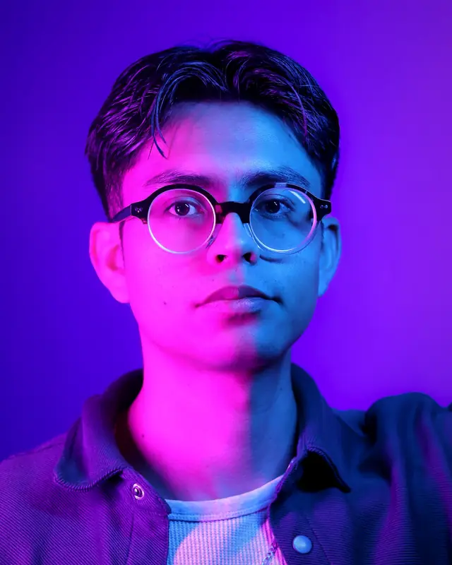 A young man in glasses bathed in violet and magenta light