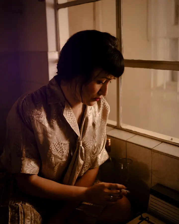 A person sitting by a window in a dim room, lost in thought